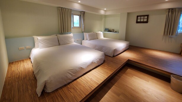 A hotel room with two beds, a wooden floor, a small table, and a window with curtains. - Stay a moment inn (Luodong)