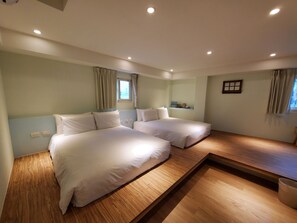 A hotel room with two beds, a wooden floor, a small table, and a window with curtains. - Stay a moment inn (Luodong)