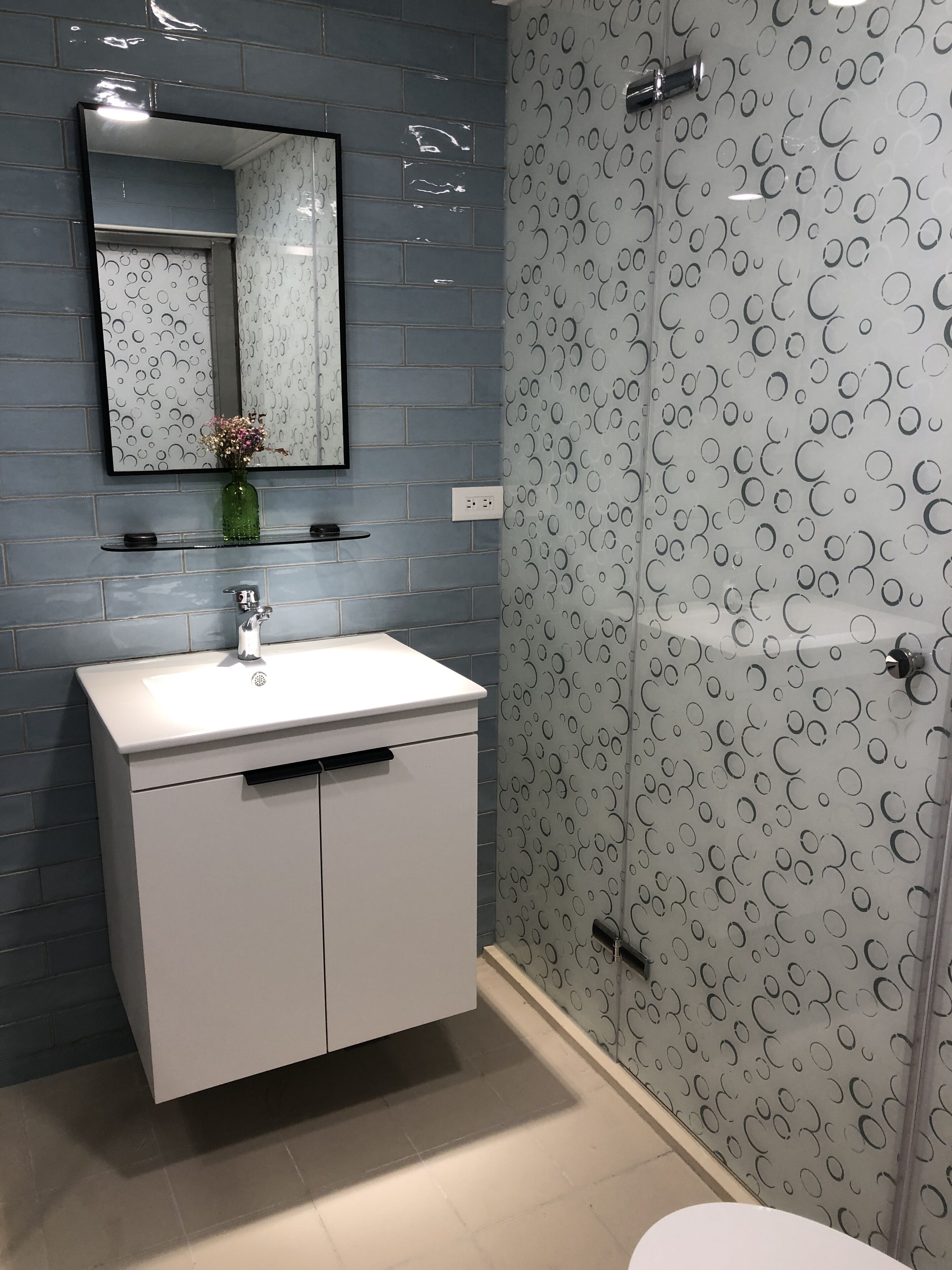 A bathroom with a white sink, mirror, and a shower with a circular pattern wall.