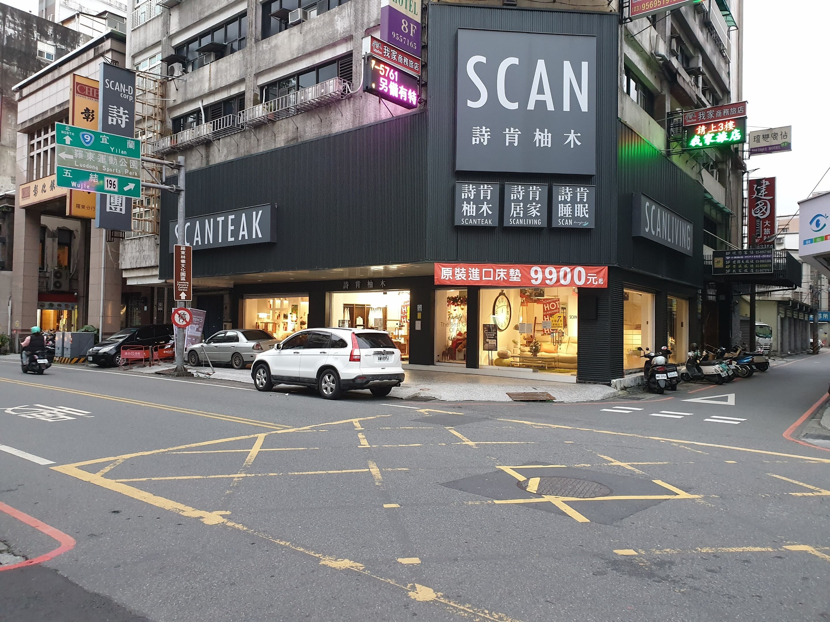 Un edificio con un gran letrero que dice 'SCAN', un restaurante 'SCANTEAK' y una tienda 'SCANLIVING'.