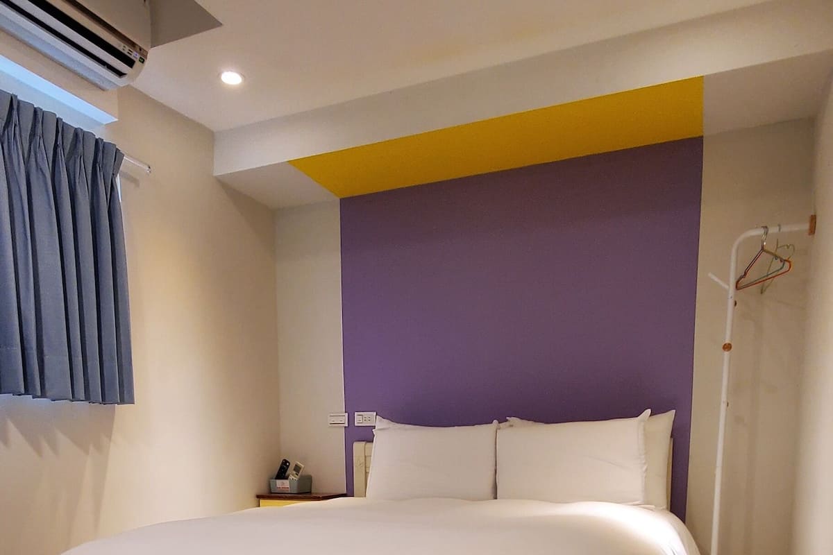 Une chambre d’hôtel moderne avec un grand lit, une table de chevet et un climatiseur fixé au mur.