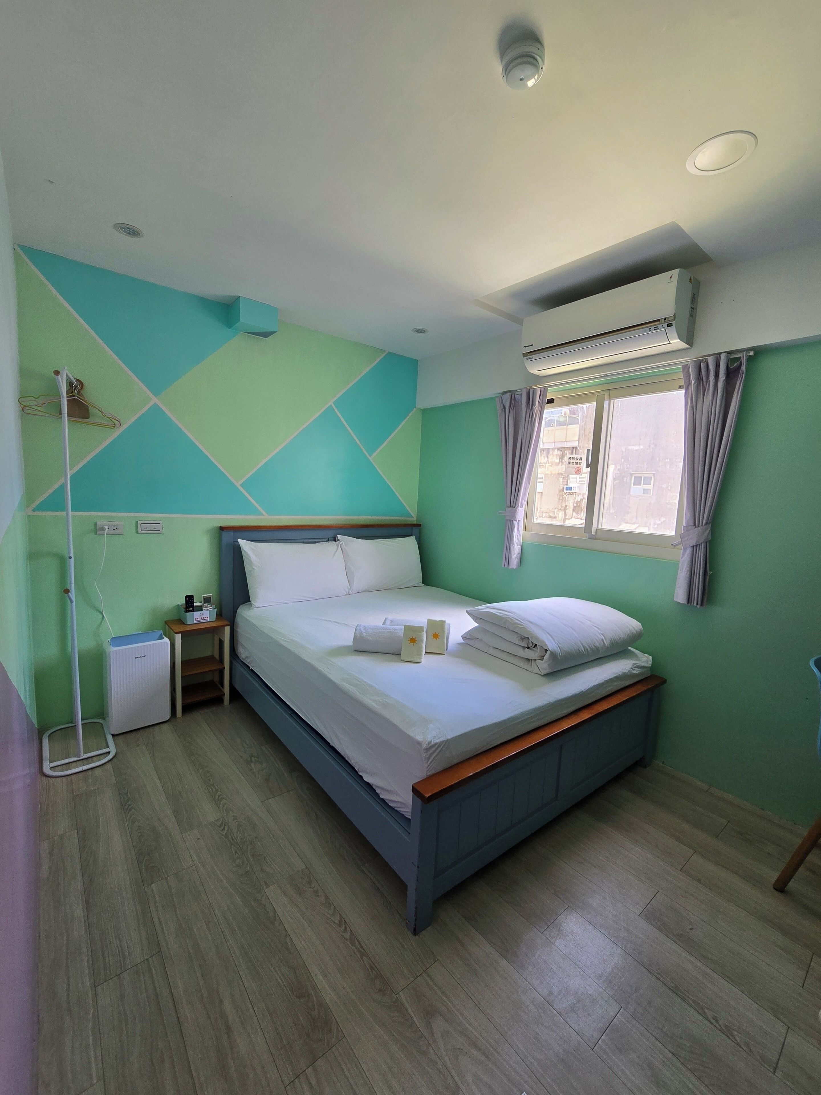 A neatly made bed with white linens, a bedside table with a lamp, and a window with curtains.