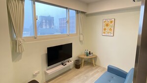 A modern living room with a flat-screen TV, a blue sofa, a small round table with bottles, and a window with curtains. - Stay a moment inn (Luodong)