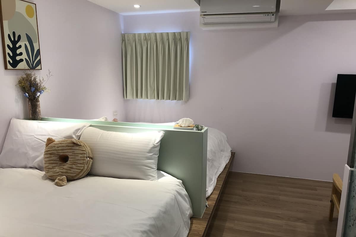 Une chambre d’hôtel avec deux lits, un téléviseur à écran plat, un climatiseur et une fenêtre avec des rideaux.