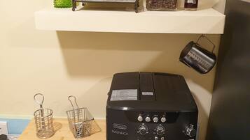 A coffee machine on a table with a shelf above it holding a metal rack, jars, and a bottle.