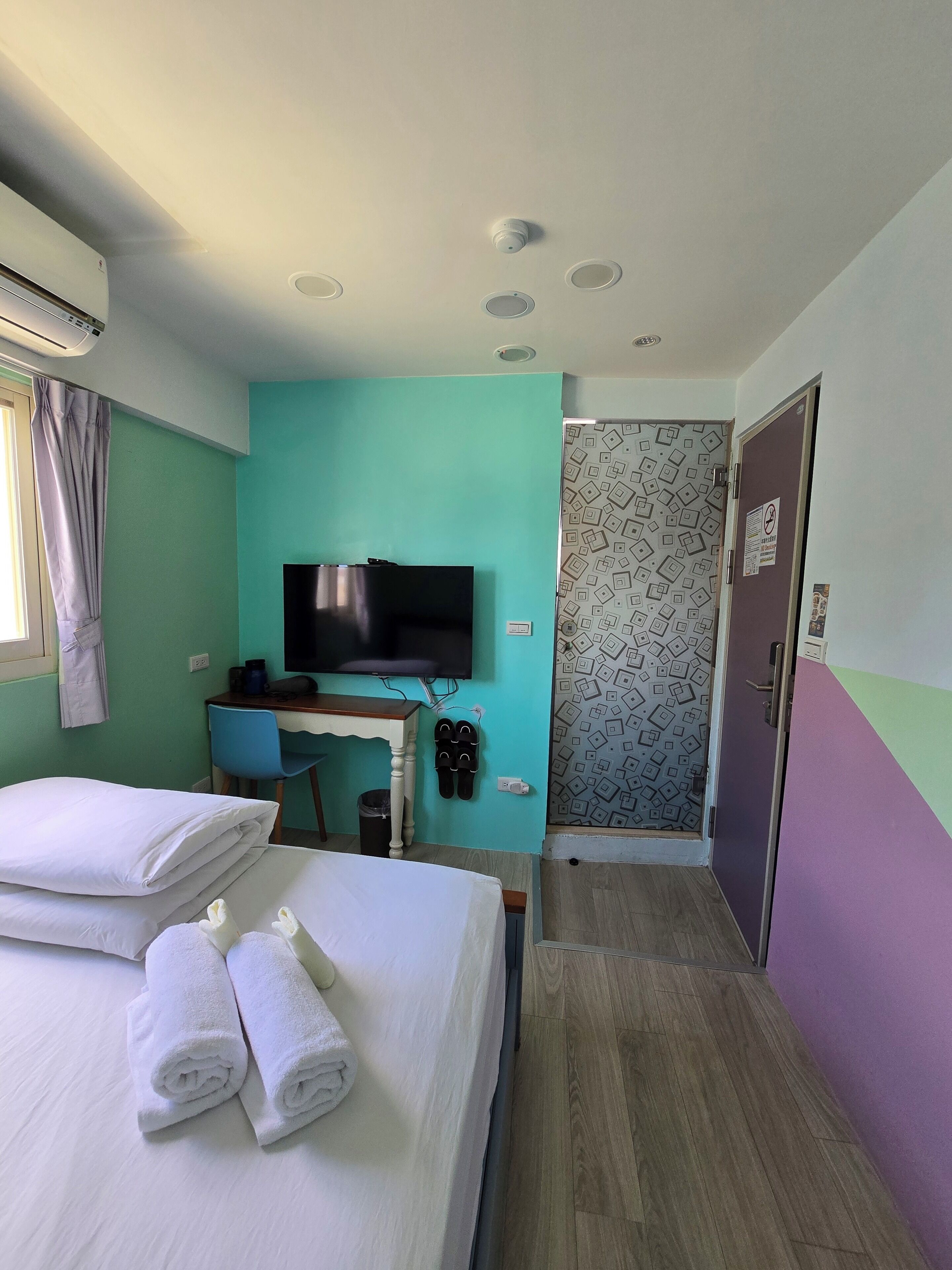 A hotel room with a bed, a desk, a TV, and a shower area.