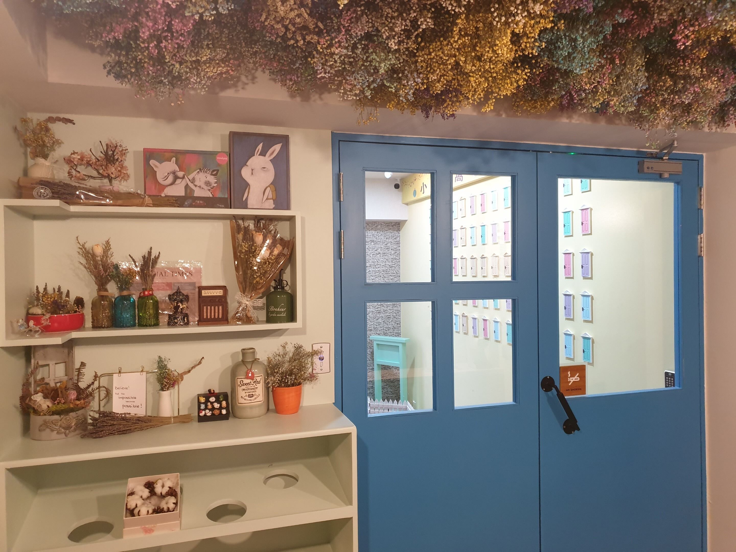 A room with a blue door, shelves with various decorative items, and a view of colorful buildings through the door.