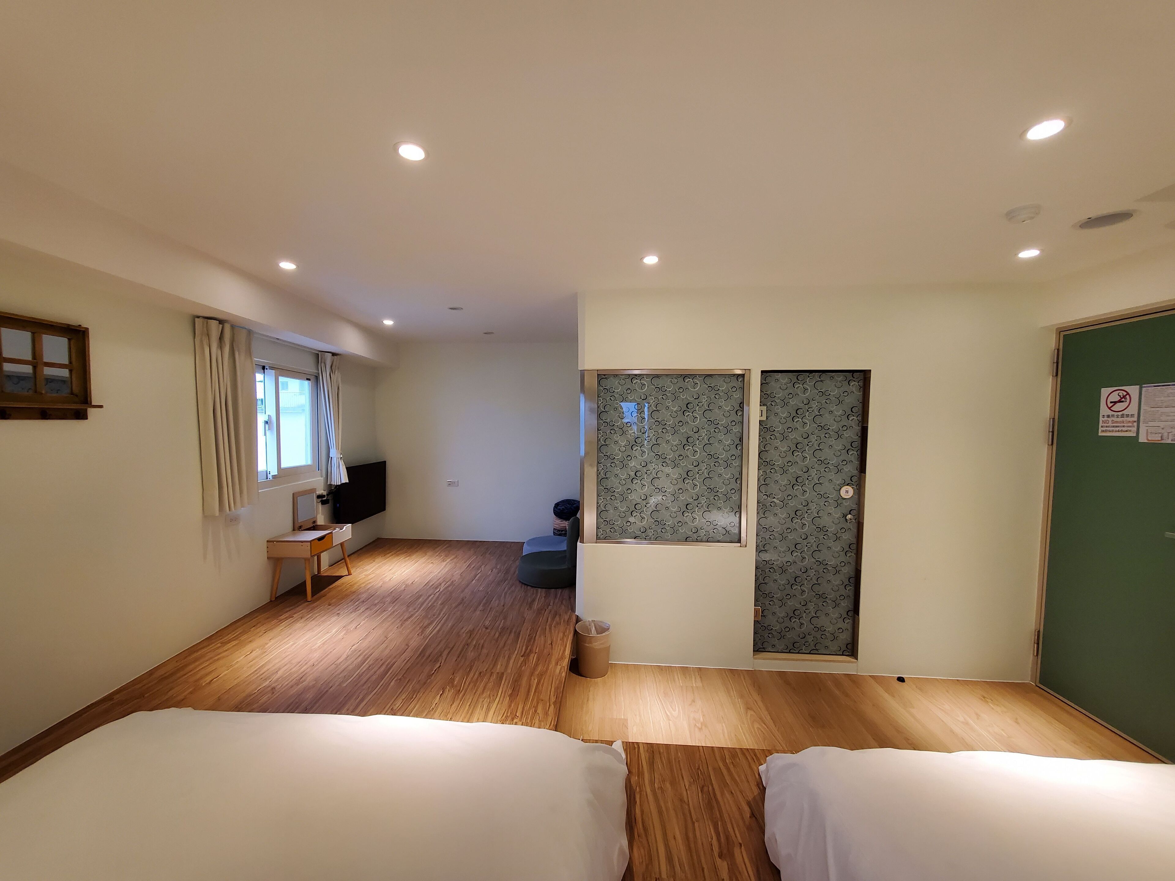 Quarto de hotel com duas camas, piso de madeira, televisão, janela com cortinas e porta verde com tranca.