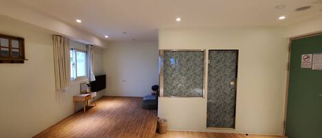Habitación de hotel con dos camas, suelo de madera, televisor, ventana con cortinas y puerta verde con cerradura.