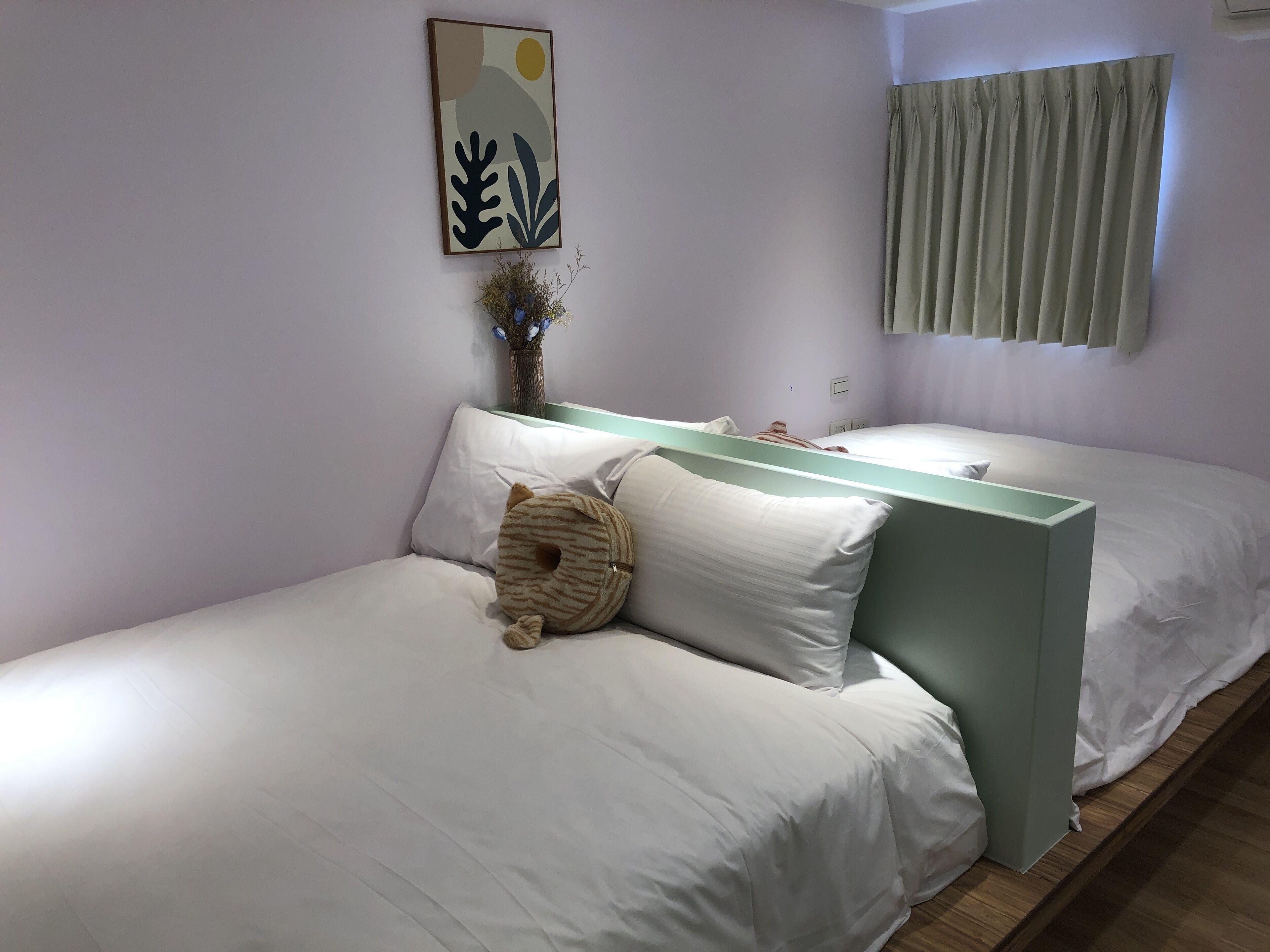 A bedroom with two beds, a bedside table with a vase, and a wall-mounted artwork.