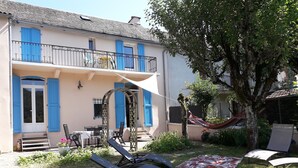 Een huis met twee verdiepingen, een balkon, buitenmeubilair en een hangmat.
