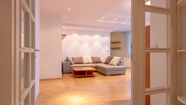 Uma sala de estar moderna com um sofá modular, uma mesa de centro de madeira e iluminação embutida no teto.