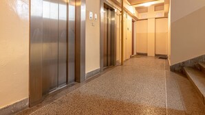Um corredor com quatro elevadores, piso coberto de carpete e escada à direita.