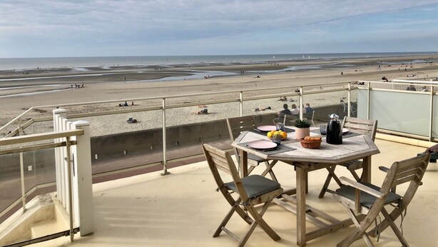 A balcony with a table and chairs overlooking a beach.