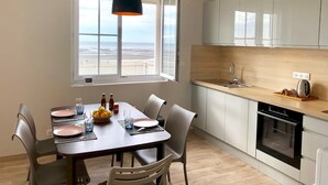 A modern kitchen with a view of the beach, a dining area with a table set for two, and a large window.