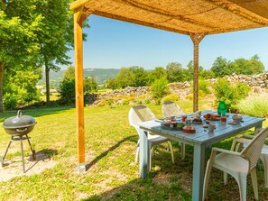 An outdoor dining area with a table set for a meal, surrounded by chairs, under a thatched roof. - Renovated farmhouse in quiet area with private parking and free Wifi in Saint-Étienne-Lardeyrol (Saint-Étienne-Lardeyrol)