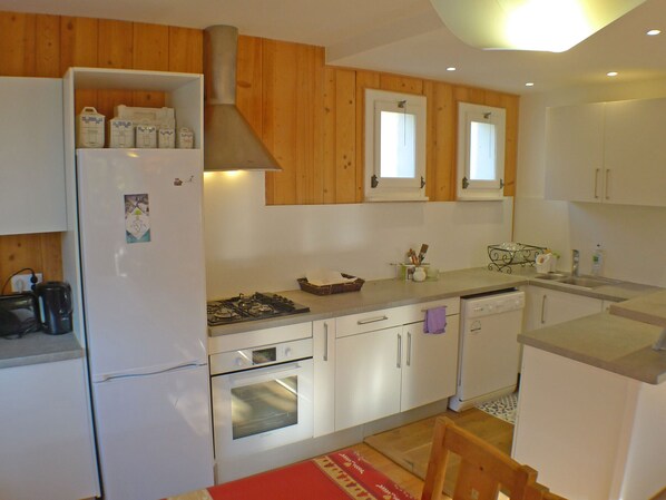 Een compacte keuken met houten kastjes, een ingebouwde oven, een kookplaat en een koelkast.