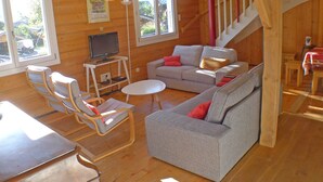 L’intérieur chaleureux d’un chalet avec un canapé, des fauteuils, une petite table, un téléviseur et un escalier.