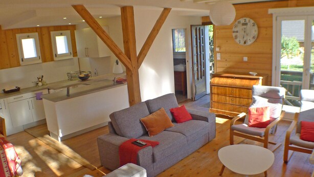 Un vaste espace de vie comprenant un canapé gris, une table à manger en bois et une cuisine à l’arrière-plan.