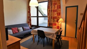 Ein gemütliches Zimmer mit einer Couch, einem Esstisch mit Stühlen, einer Lampe und einem Fenster mit Vorhängen.