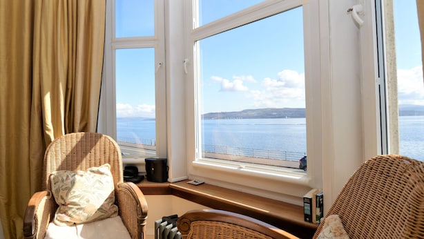 A room with a view of the sea, wicker furniture, and a window with curtains.
