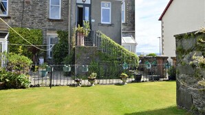 A stone house with a front door, a small porch, and a fenced garden area with potted plants.