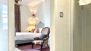 A hotel room with a bed, a chair, a lamp, and a shower area.