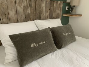 Un lit avec une literie blanche et deux oreillers gris foncé ornés d’un motif brodé.