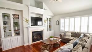 A spacious living room with a fireplace, a large flat-screen TV, a sectional sofa, and a wooden coffee table. - Beautiful townhome for a great Family vacation! (Cape Charles)