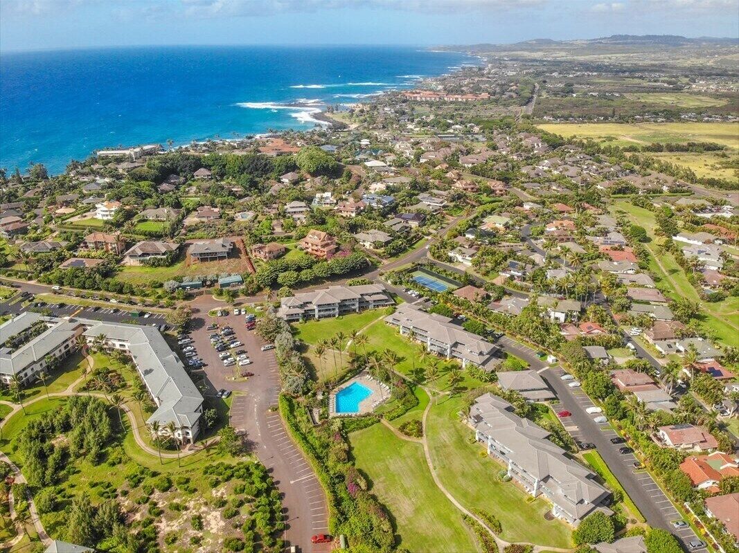 Vue aérienne d’un quartier résidentiel situé sur la côte, avec un grand complexe hôtelier comprenant plusieurs bâtiments, une piscine et un parking.