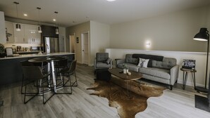 A modern kitchen with stainless steel appliances, a dining area with a round table and chairs, a grey sofa, and a large brown leather rug. - Gorgeous south facing 3BDR townhome! (Canmore)