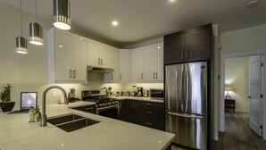 A modern kitchen with stainless steel appliances, a granite countertop, and pendant lighting. - Gorgeous south facing 3BDR townhome! (Canmore)