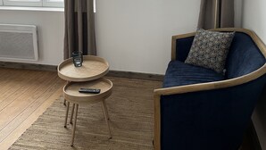 Ett modernt vardagsrum med en blå soffa, ett runt bord med en fjärrkontroll och ett fönster med gardiner.