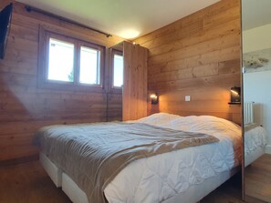 Ein Schlafzimmer mit Holzwänden, einem Bett, zwei Fenstern und Wandleuchten.
