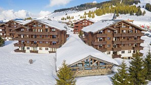 A snow-covered mountain resort with wooden buildings featuring balconies and large windows.