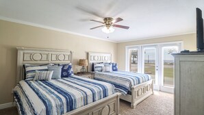 Une chambre avec deux lits, un ventilateur de plafond, une télévision et une vue sur l’extérieur grâce à une porte coulissante.