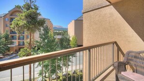 Ein Balkon mit Korbstuhl und Blick auf ein Gebäude, im Hintergrund ein Berg.