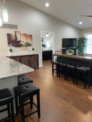 A modern kitchen with a granite countertop, black bar stools, and a dining area with a black table and chairs. - A Stunning Home, newly constructed & furnished (Hermann)