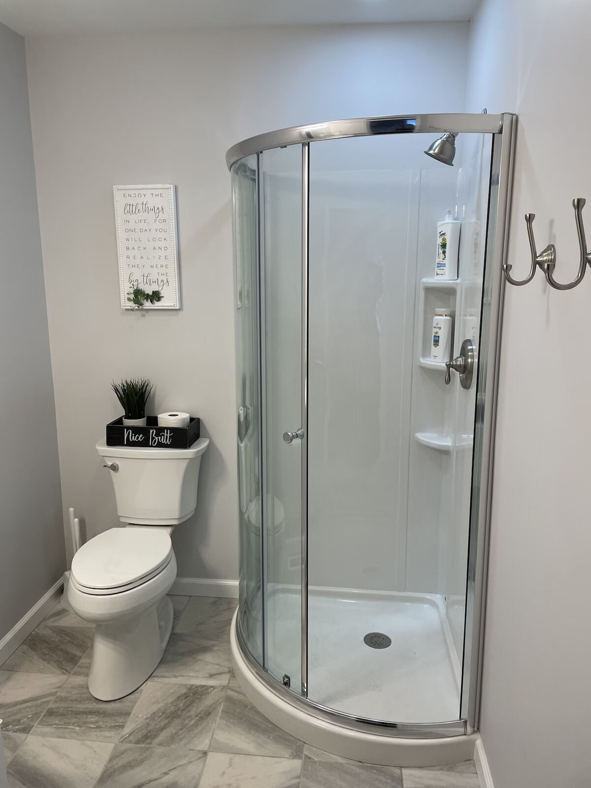 A modern bathroom with a glass-enclosed shower, a toilet, and a small shelf with toiletries.