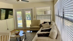 A living room with a beige sofa, a small round table with a bowl of snacks, a chair, and a television mounted on the wall. - Beautiful Spacious 3 bedroom home near Clearwater Beach, Pet friendly! (Clearwater)