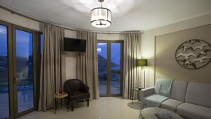 A modern living room with a sofa, a chair, a coffee table, a TV mounted on the wall, and a balcony with curtains. - Villa Mare with Private Pool and Sea Views (Vasiliki)