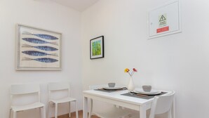 Un área de comedor con una mesa y sillas blancas, una obra de arte enmarcada de peces y una fotografía en la pared.