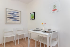Un coin repas avec une table et des chaises blanches, une œuvre d’art encadrée représentant des poissons et un tableau encadré accroché au mur.
