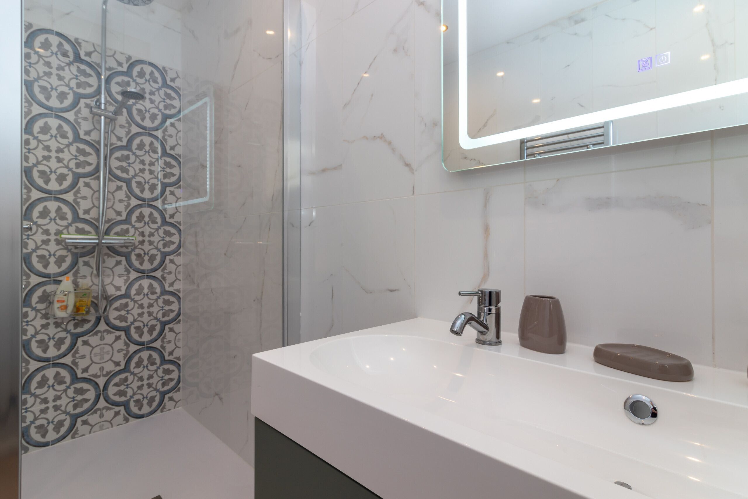 A modern bathroom with a white sink, a mirror, and a shower with patterned tiles.