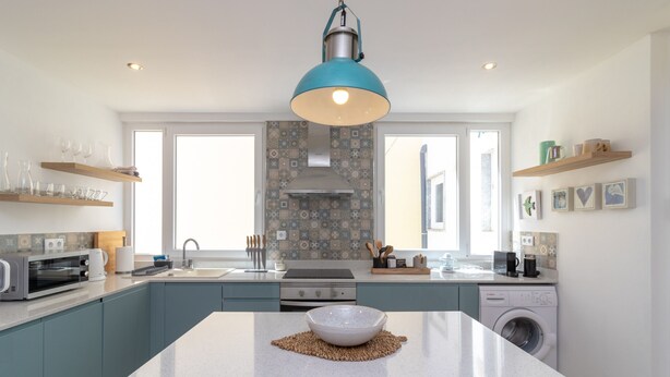 Una cocina moderna con una isla central, electrodomésticos integrados y una lámpara colgante.