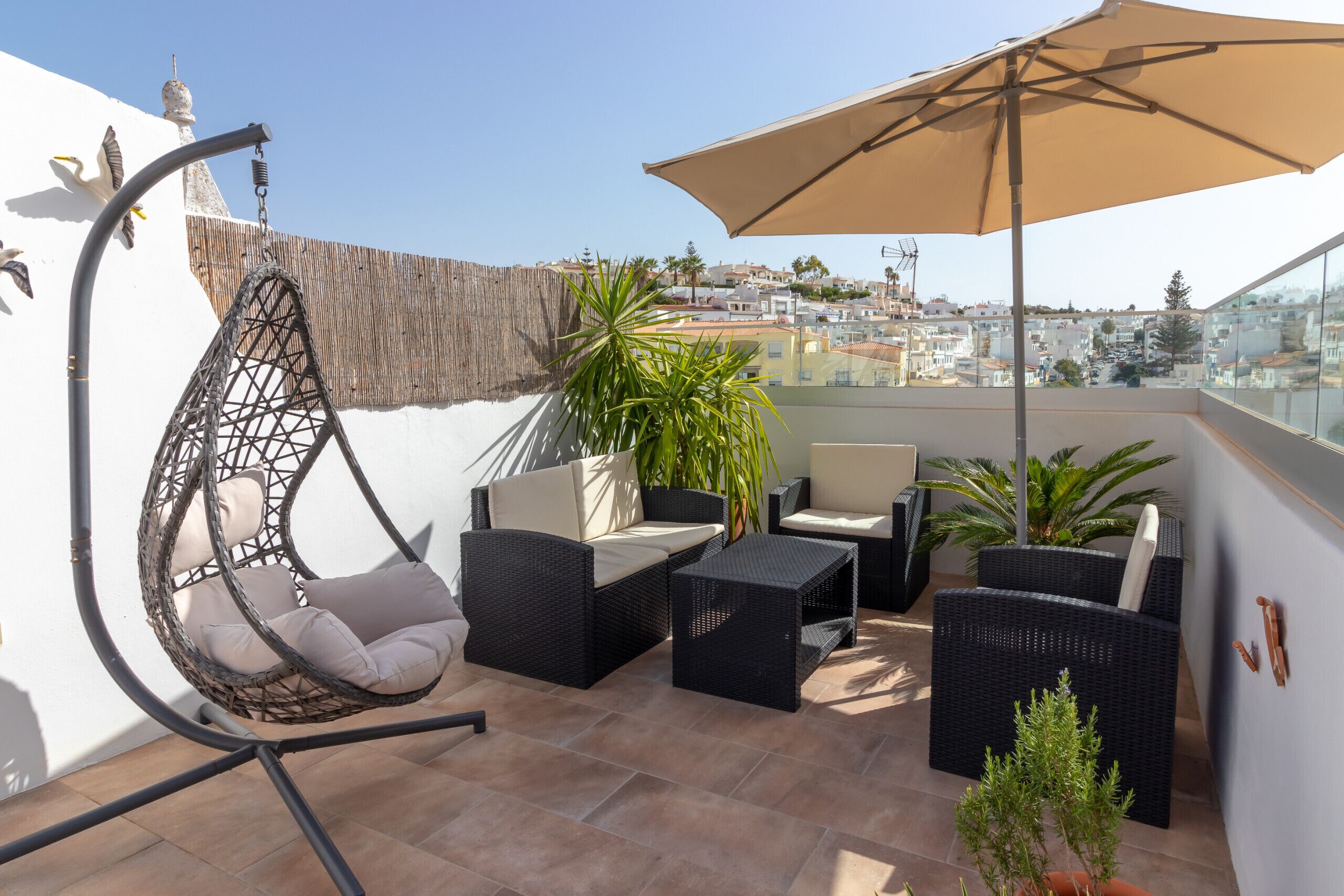 A rooftop terrace with wicker furniture, a hanging chair, and a large umbrella.