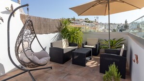 Terraza en la azotea con mobiliario de mimbre, una silla colgante y un paraguas grande.