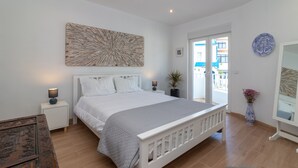 Un dormitorio con una cama grande, una mesita de noche, una lámpara de noche, una obra de arte en la pared, una planta en maceta y vistas al exterior.