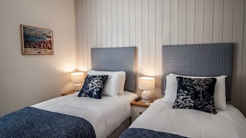 A hotel room with two beds, each with a headboard, bedside lamps, and decorative pillows. A framed picture hangs on the wall.