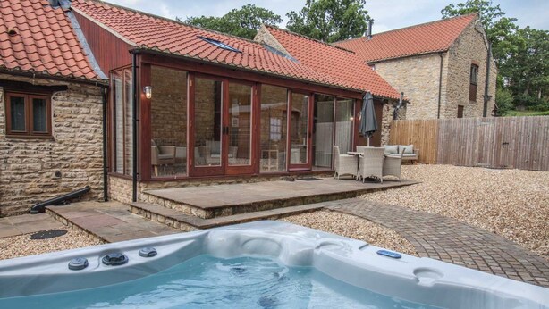 Ein Whirlpool in einem Hinterhof mit einem Steinhaus und einer überdachten Terrasse.